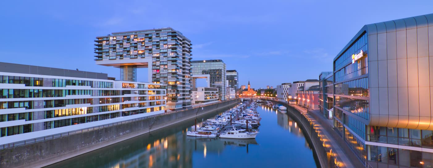 Rheinauhafen Köln in Abendstimmung. Links sieht man die Kranenhäuser. Mittig sieht man Boote im Rheinauhafen liegen. Das Wasser ist glatt. Rechts im Bild steht das Microsoft Gebäude der Niederlassung Köln.