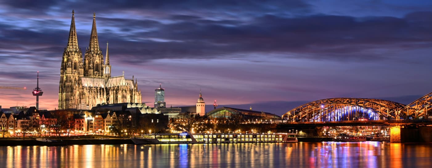 Köln bei Nacht. Links im Bild sieht man den angestrahlten Dom. Davor die Altstadt. Das Bild wurde von der 'Schäl Sick' aus aufgenommen. Der Rhein ist durchzogen von Licht. Auf der rechten Seite sieht man die Hohenzollernbrücke die Richtung Dom zeigt.